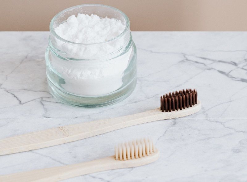 Glass jar of white powder with two toothbrushes on a marble surface