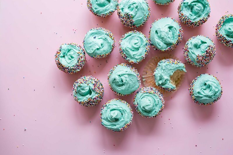 Mint-green frosted cupcakes on a pink background, arranged in a scattered cluster