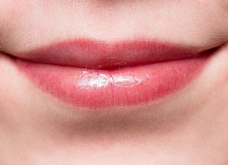 Close-up of smiling lips with glossy pink lipstick
