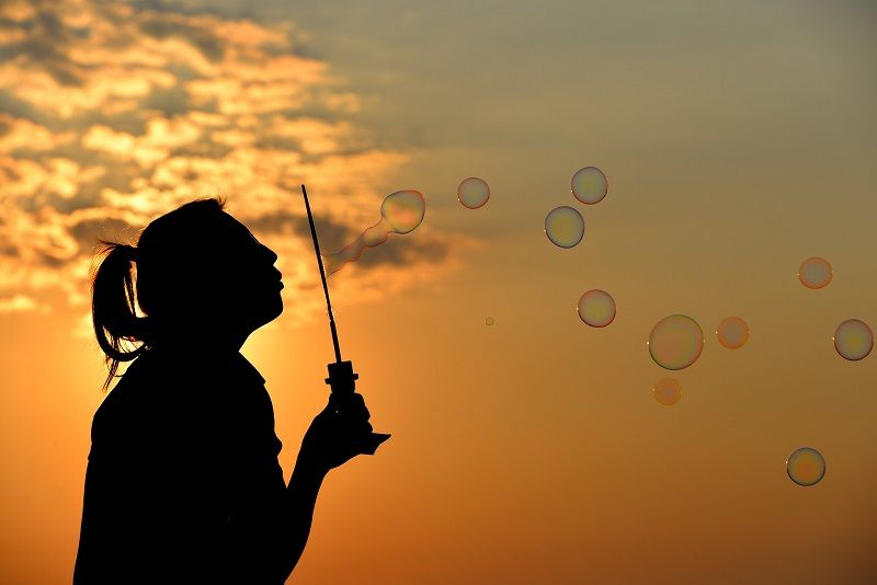 Silhouette blowing soap bubbles at sunset against an orange sky