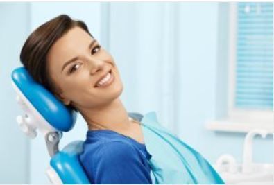 Smiling patient reclining in a blue dental chair at a bright clinic