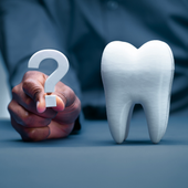 Hand holding a question mark beside a white tooth model on a blue surface