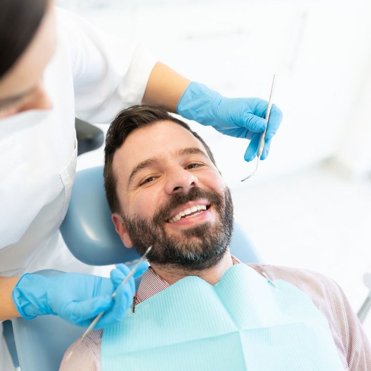 Smiling patient in a dental chair as a dentist in blue gloves examines his mouth with a mirror.