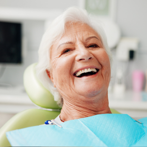 Smiling patient in a dental chair with a blue bib and green headrest
