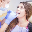 Dentist examining a patient’s mouth with dental tools while wearing gloves and a mask.