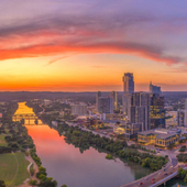 Sunset over a city river with a glowing orange sky and high-rise buildings