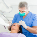 Dentist in blue scrubs wearing a mask, treating a patient in a dental chair with tools.
