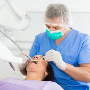 Dentist in blue scrubs wearing a mask, treating a patient in a dental chair with tools.