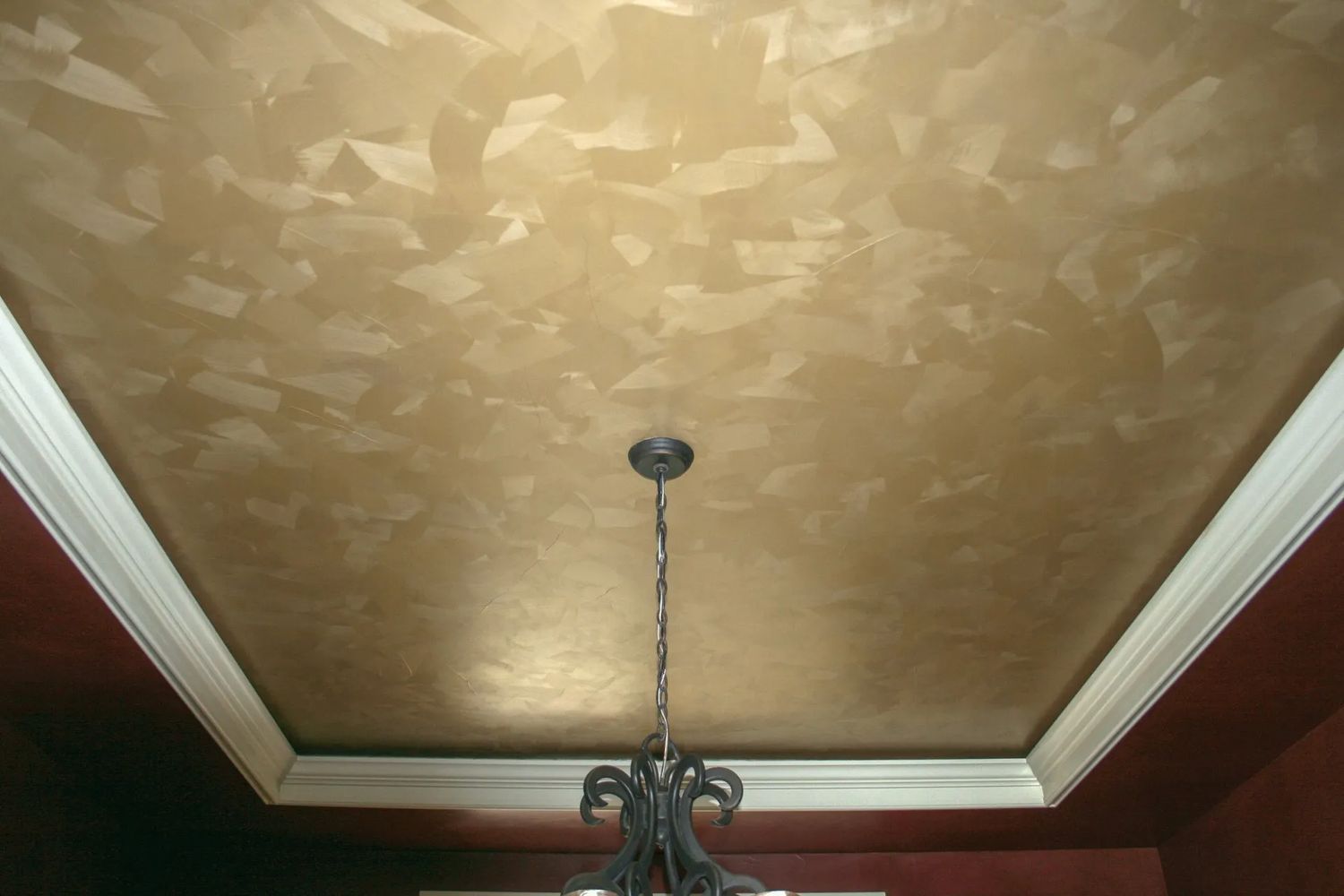 Gold textured ceiling with white trim and a chandelier.