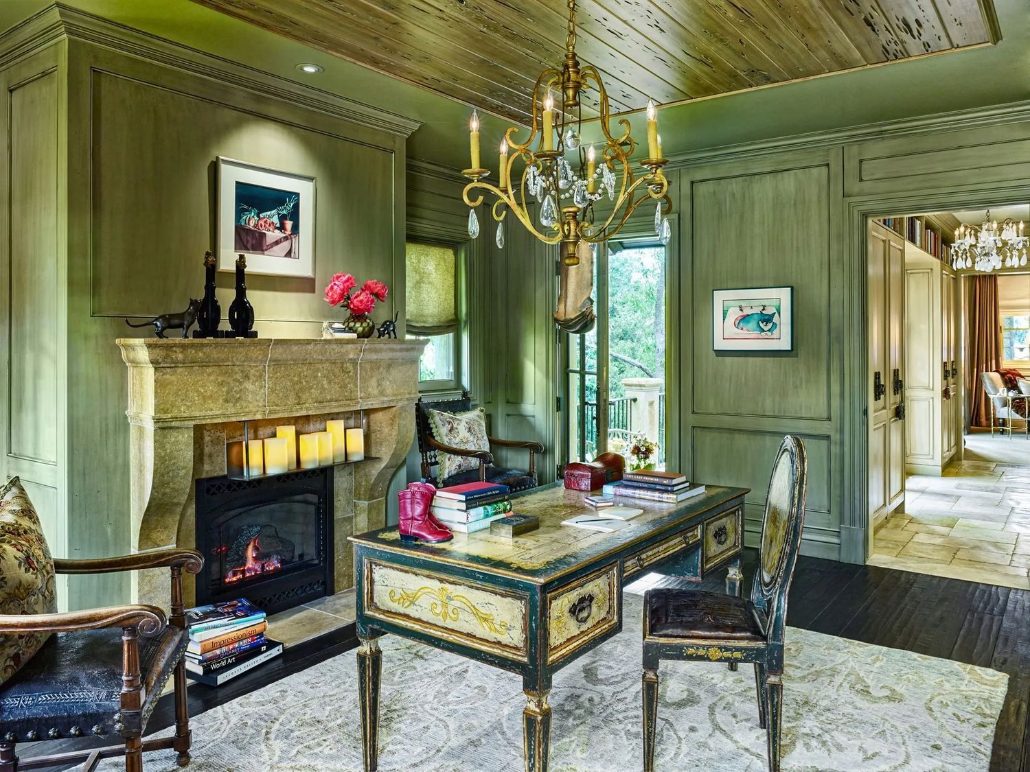 Elegant green sitting room with fireplace, chandelier, and antique desks near an open doorway
