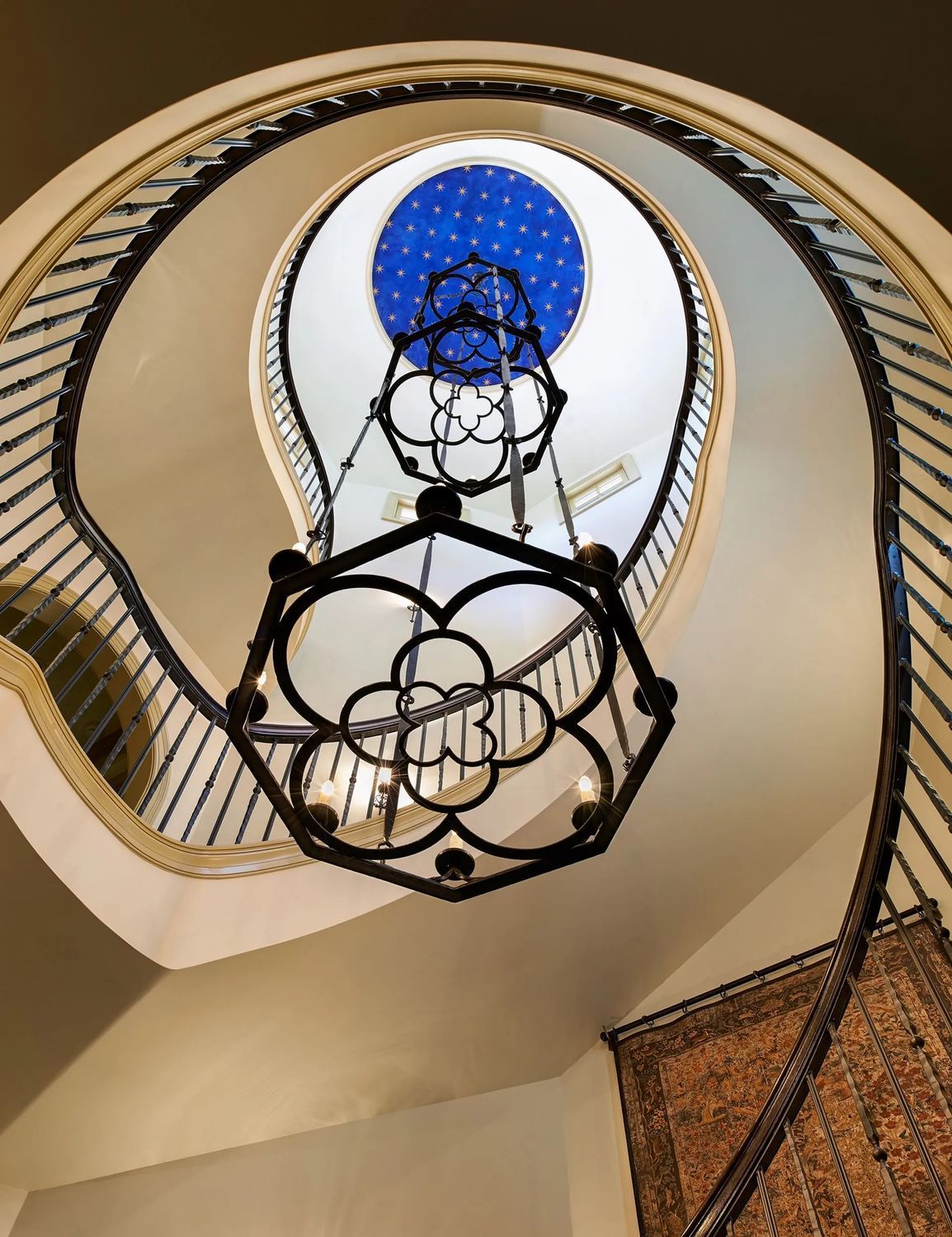 Spiral staircase with a decorative chandelier, and blue ceiling detail.