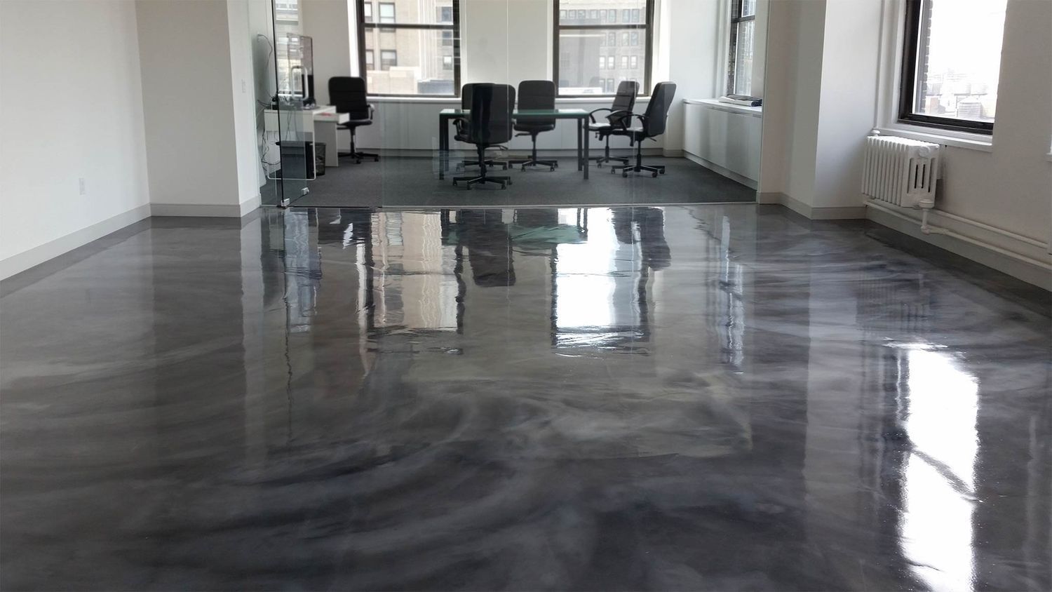 Gray metallic epoxy floor in an empty office space with chairs, a table, and windows.