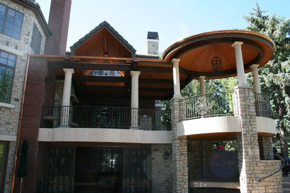 Multi-level stone and wood patio with columns, railings, and a gazebo, set against a blue sky.