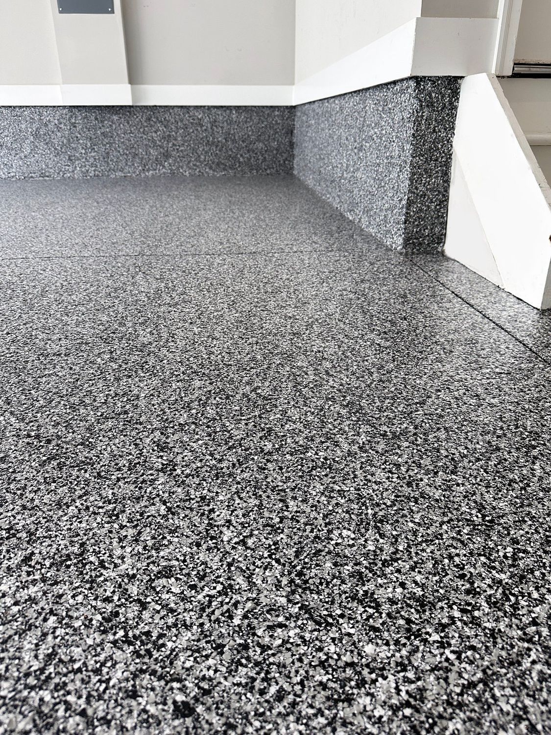 Speckled gray carpet in a corner room with white walls and a dark baseboard strip.