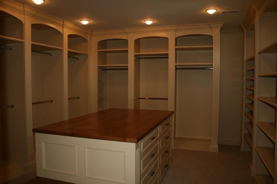 Walk-in closet with cream-colored built-in shelving and a central island with drawers and a wooden countertop.