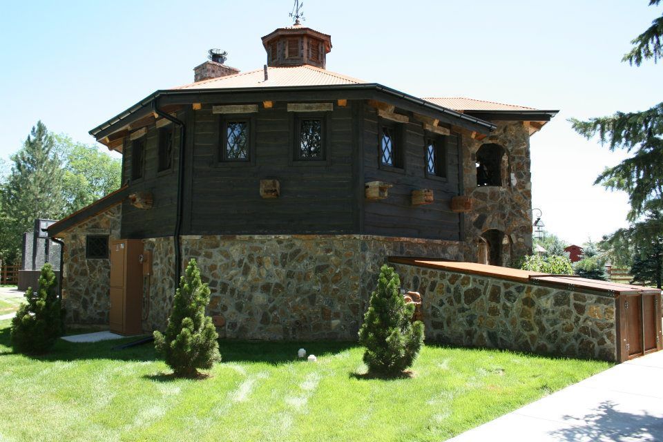 Stone and wood building with small windows, topped with a copper dome and weather vane. Green lawn, trees in sunny setting.