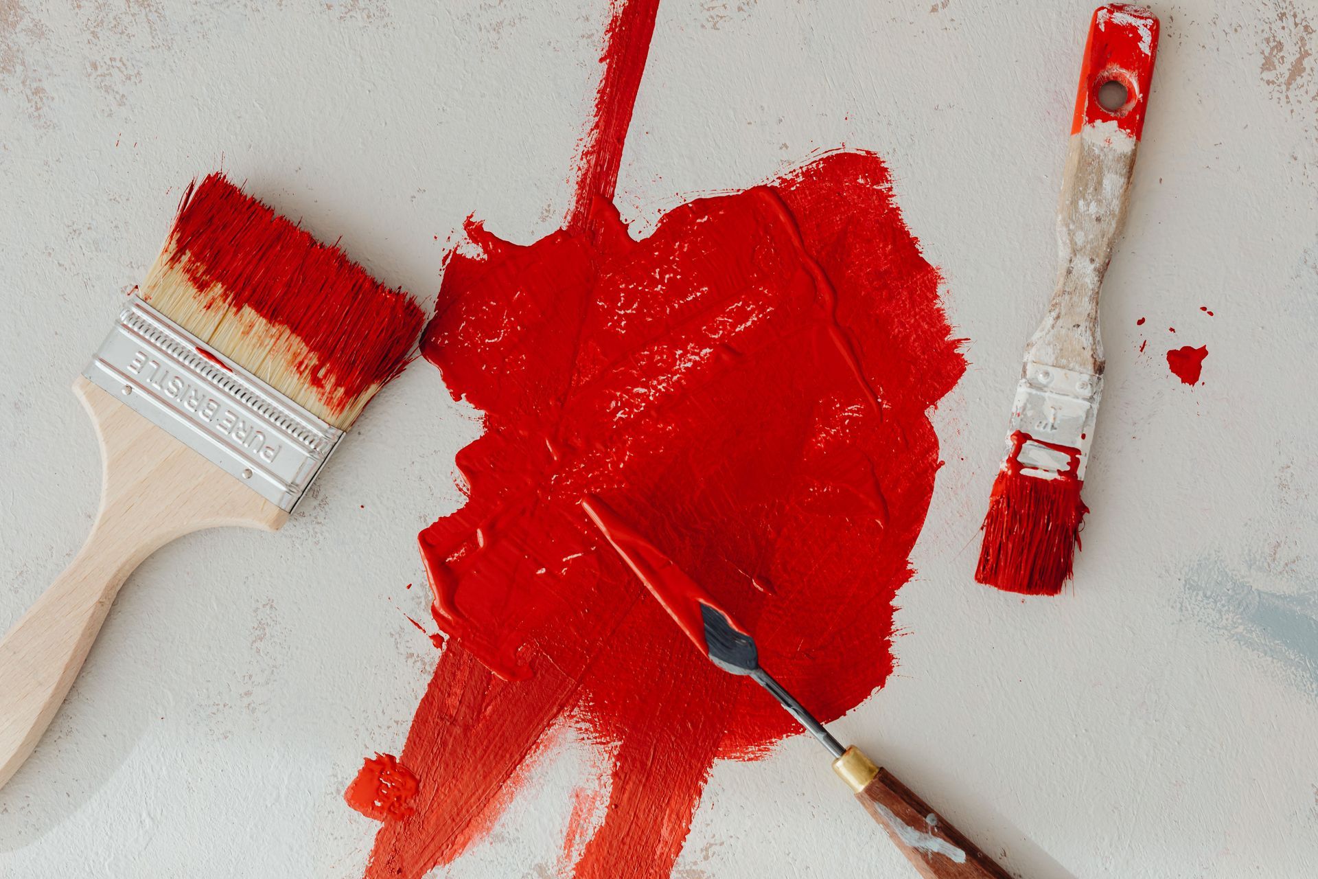 Paintbrushes and red paint smeared on a white surface.