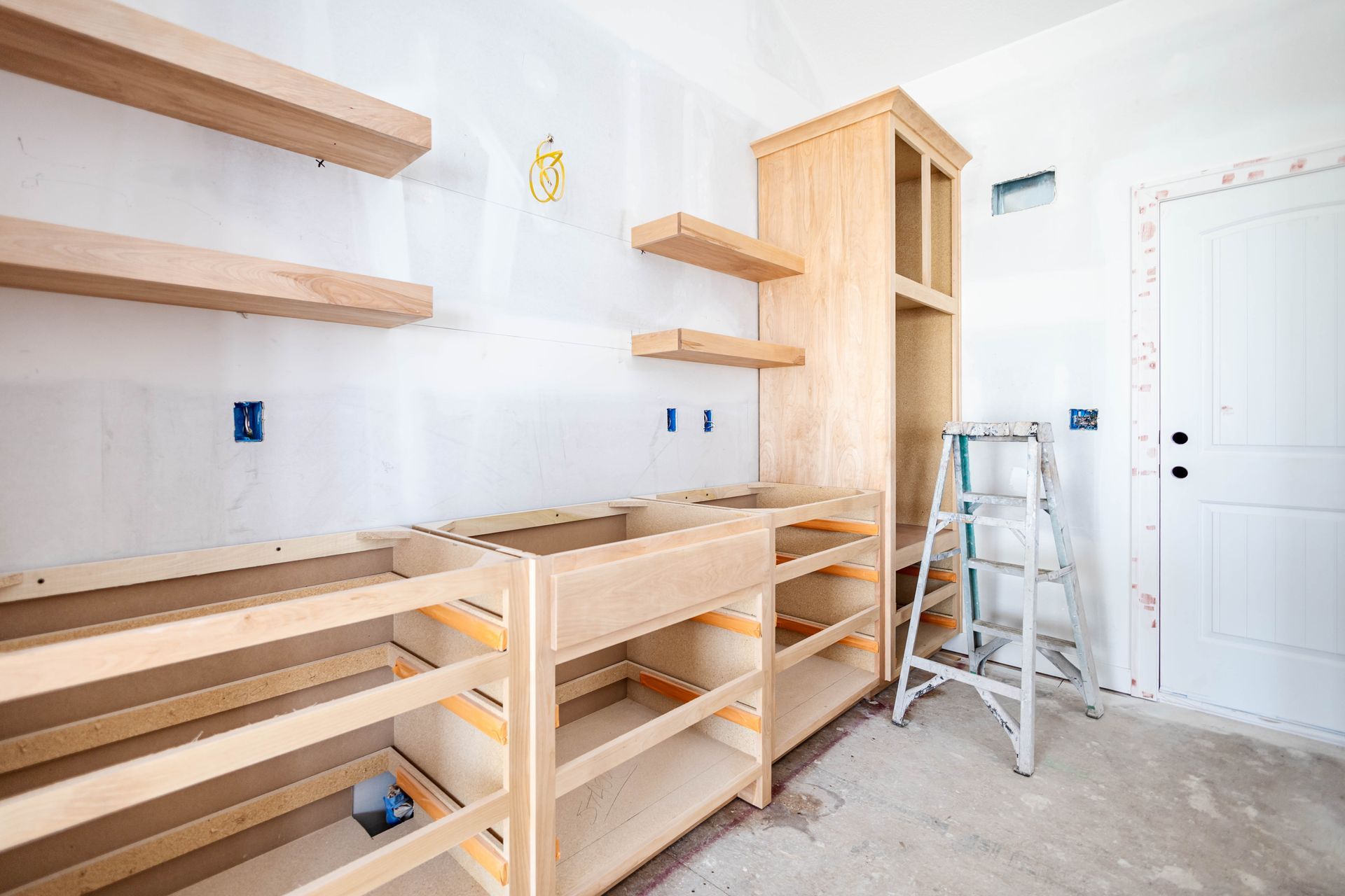 Unfinished kitchen with wood cabinets, open shelves, a ladder, and white walls under construction