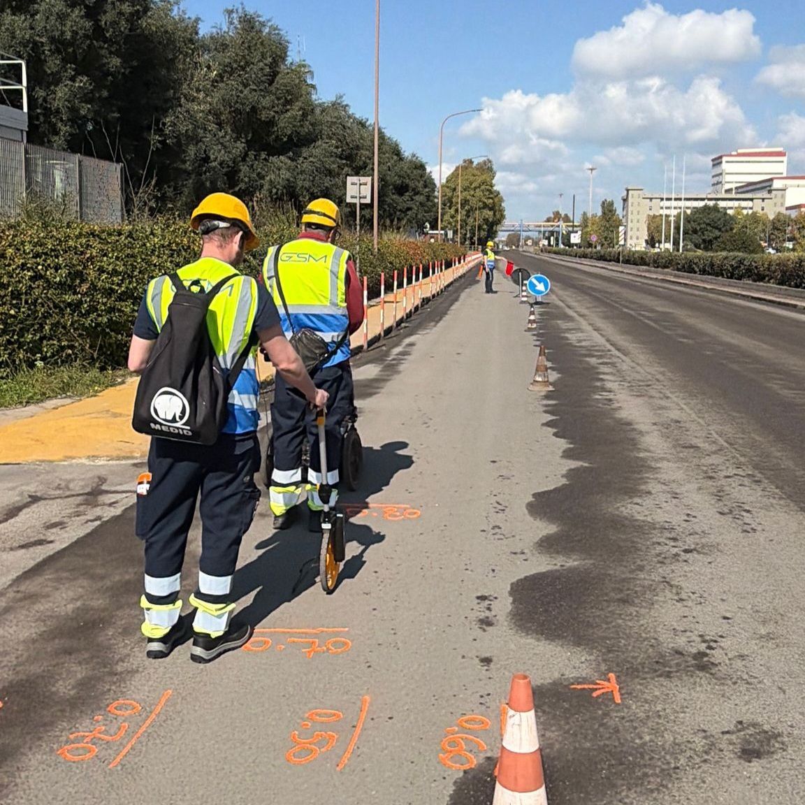 Operai con indumenti di sicurezza gialli ispezionano la segnaletica stradale con coni e attrezzature.