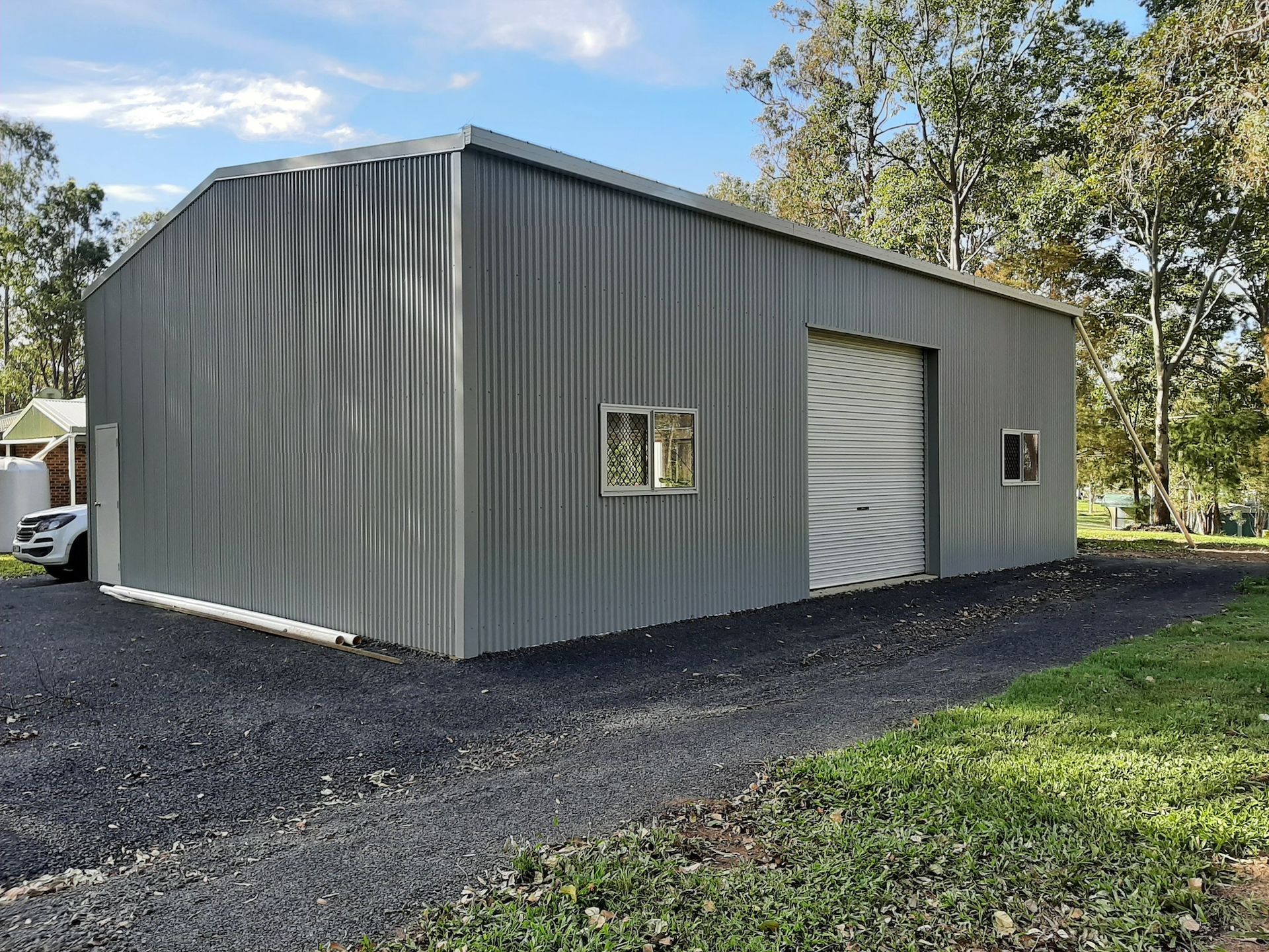 Vehicles Parked Next to a Spacious Steel  Storage Shed — Shed Kits in Lismore, NSW