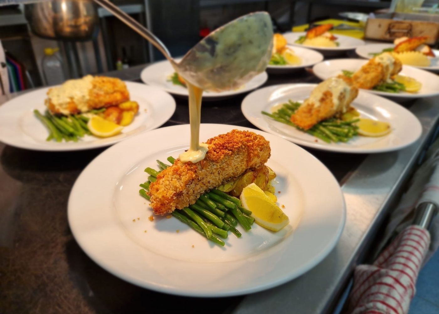 Plated crusted fish served with green vegetables and a fresh sauce being poured, showcasing high‑quality, nutritious workplace dining aligned with 2026 food trends.