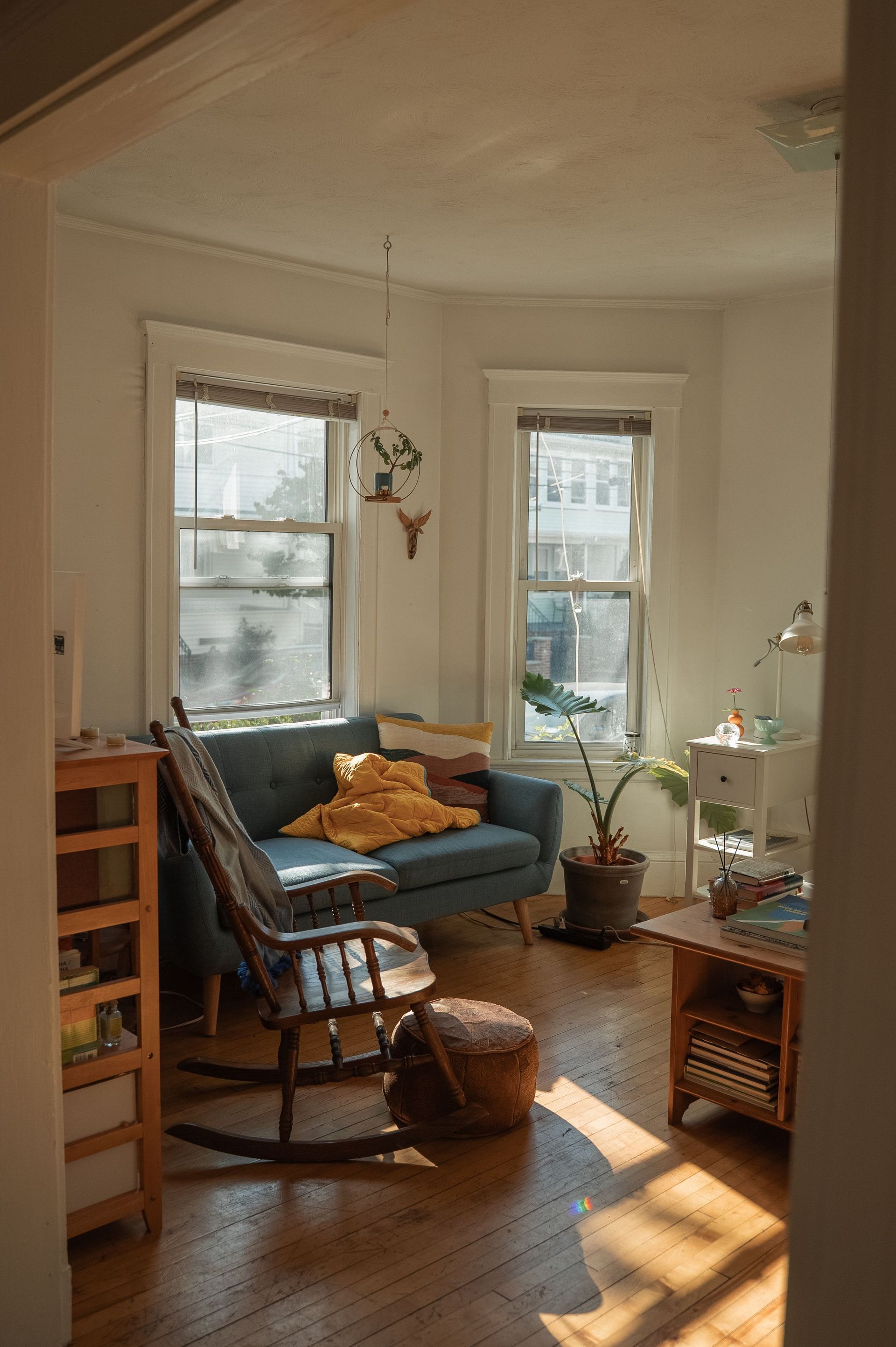 Bright living room with blue sofa, rocking chair, plants, and sunlight on wooden floor
