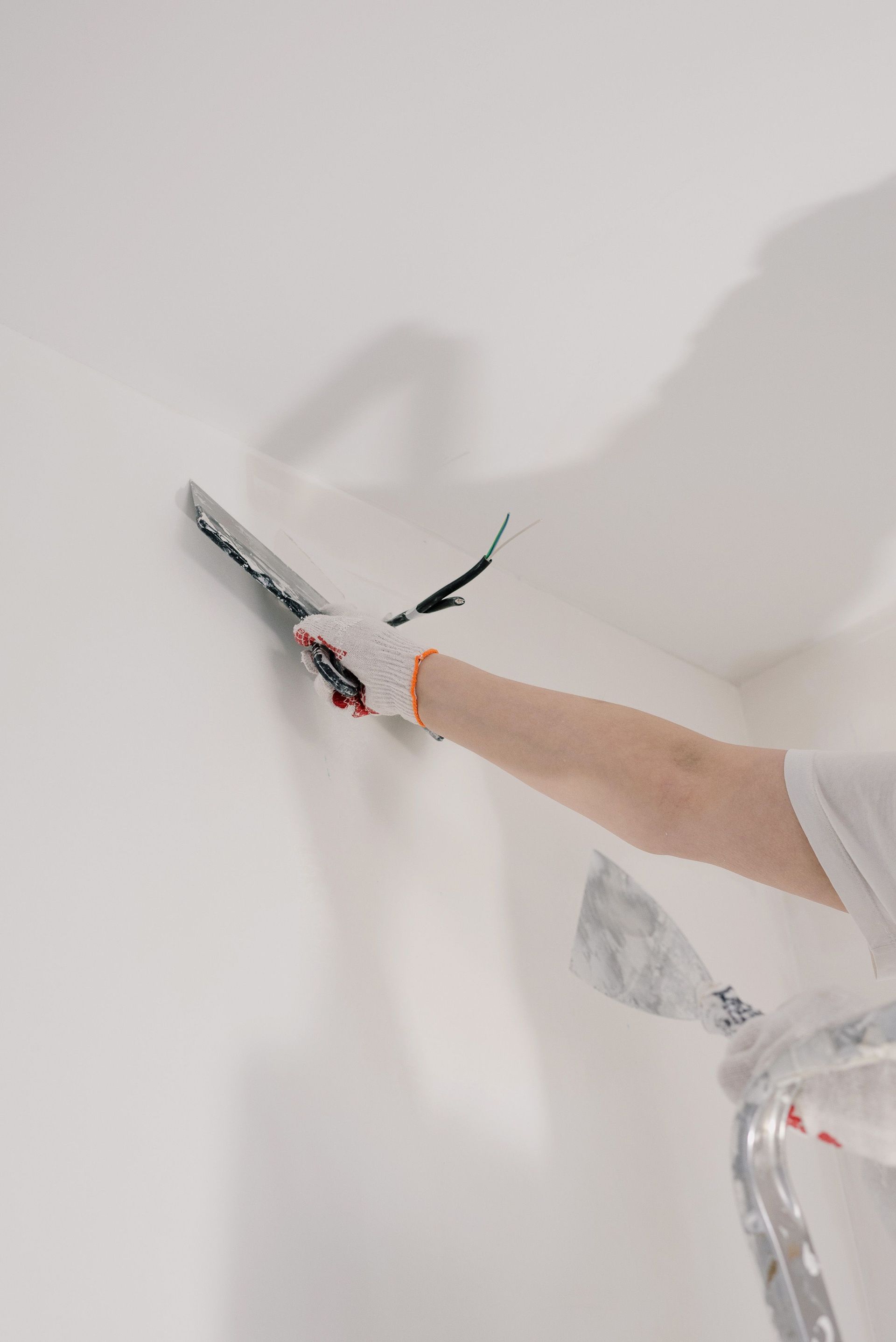 Person painting a white wall with a roller, arm extended from a paint-covered shirt