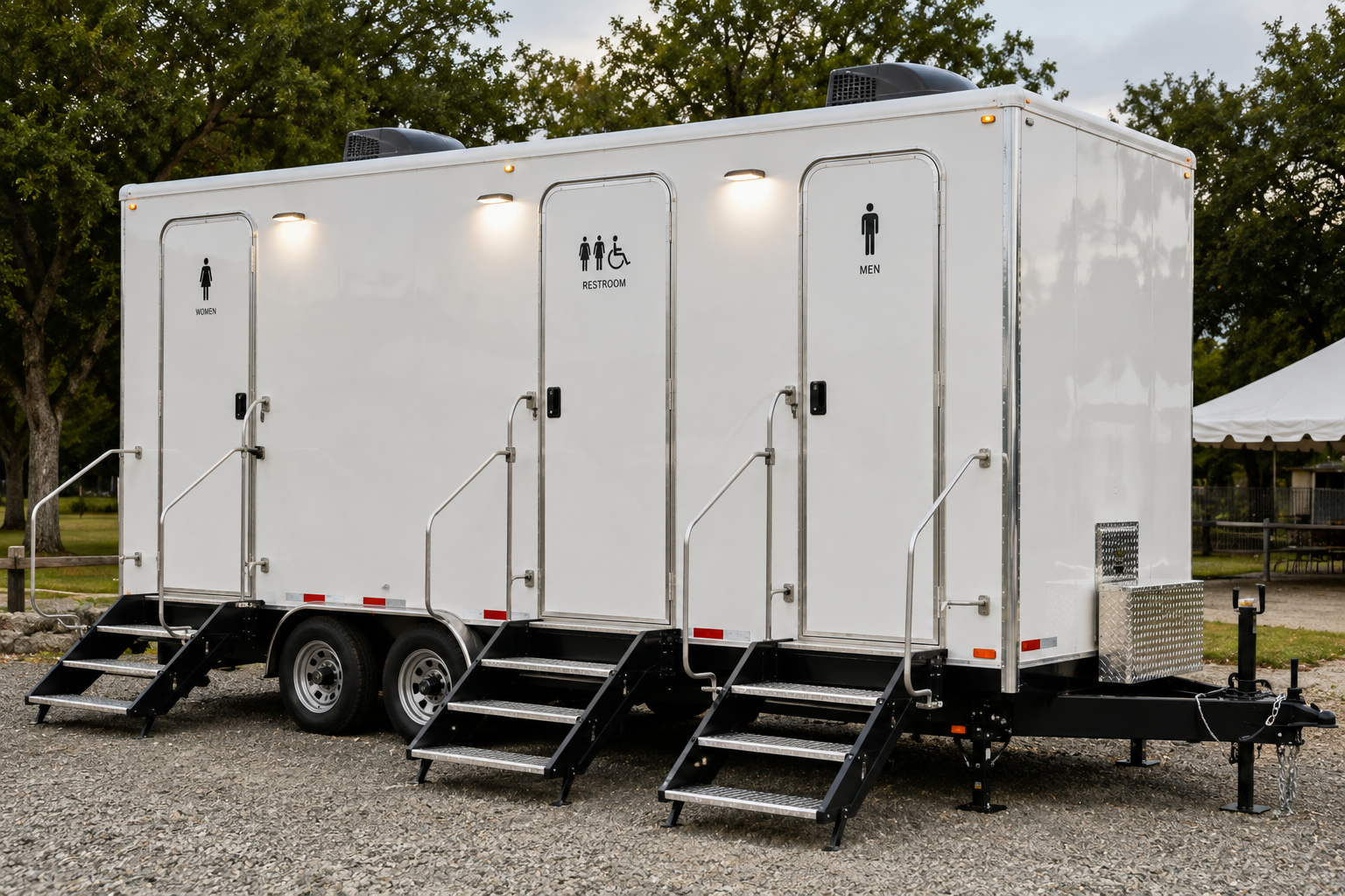 White portable restroom trailer with three doors and stairs, parked outdoors on gravel.