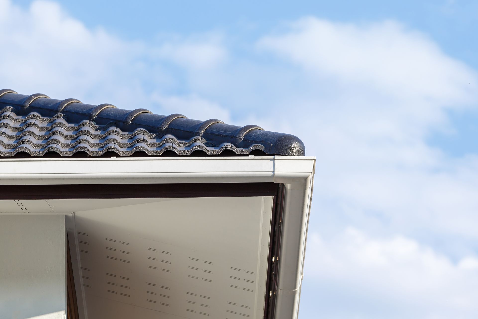 Black gutter and downspout on a white house roofline with trees in the background Black gutter and downspout on a white house roofline with trees in the background