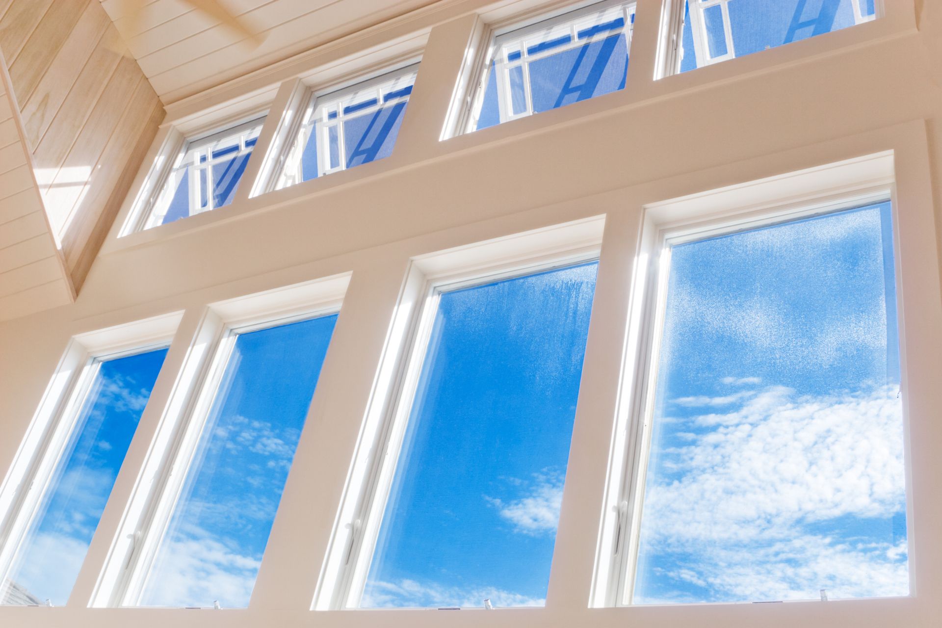 Tall white-framed windows looking up to a bright blue sky with clouds.