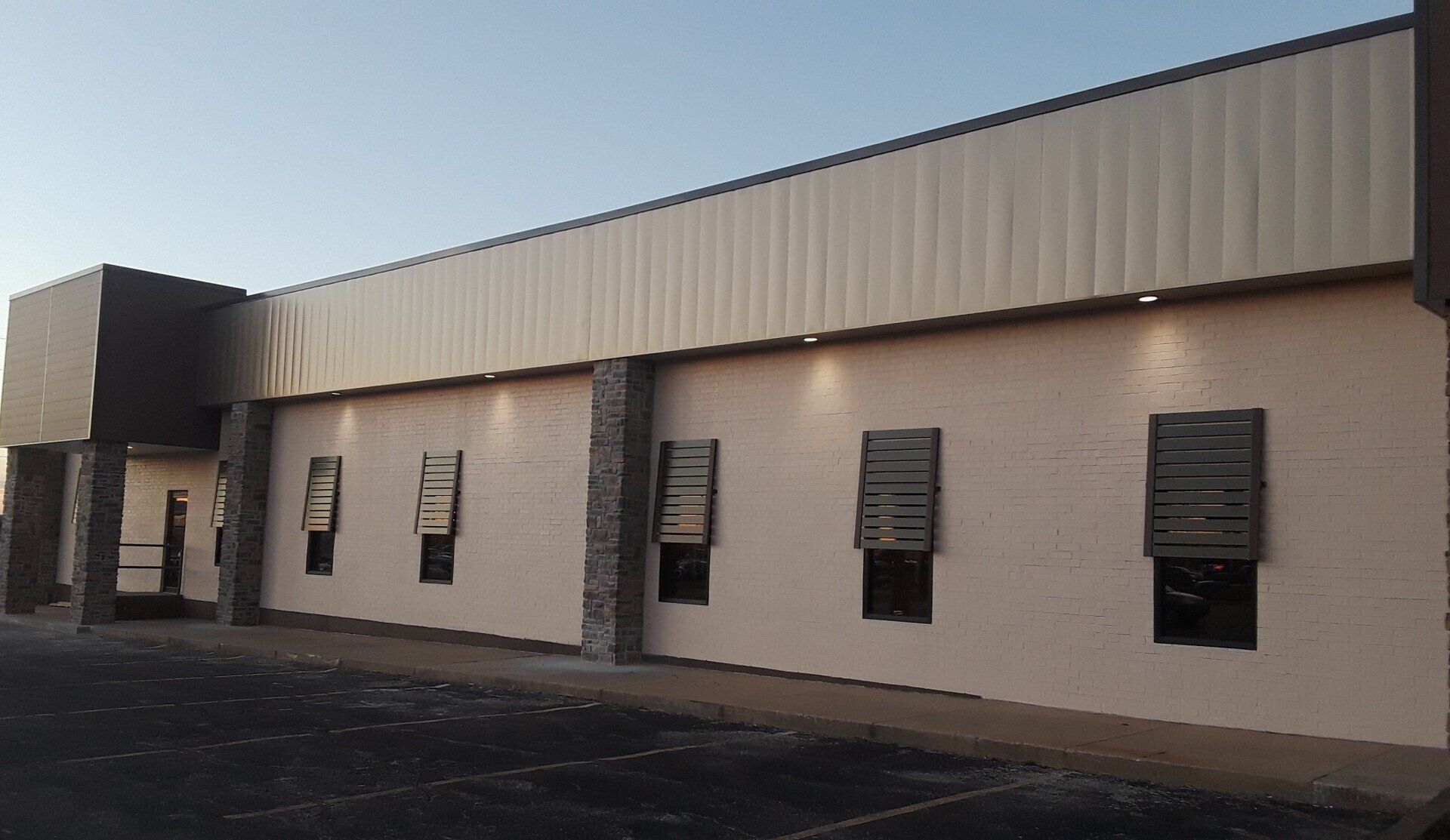 Single-story commercial building with beige brick walls, metal siding, and dark windows at dusk