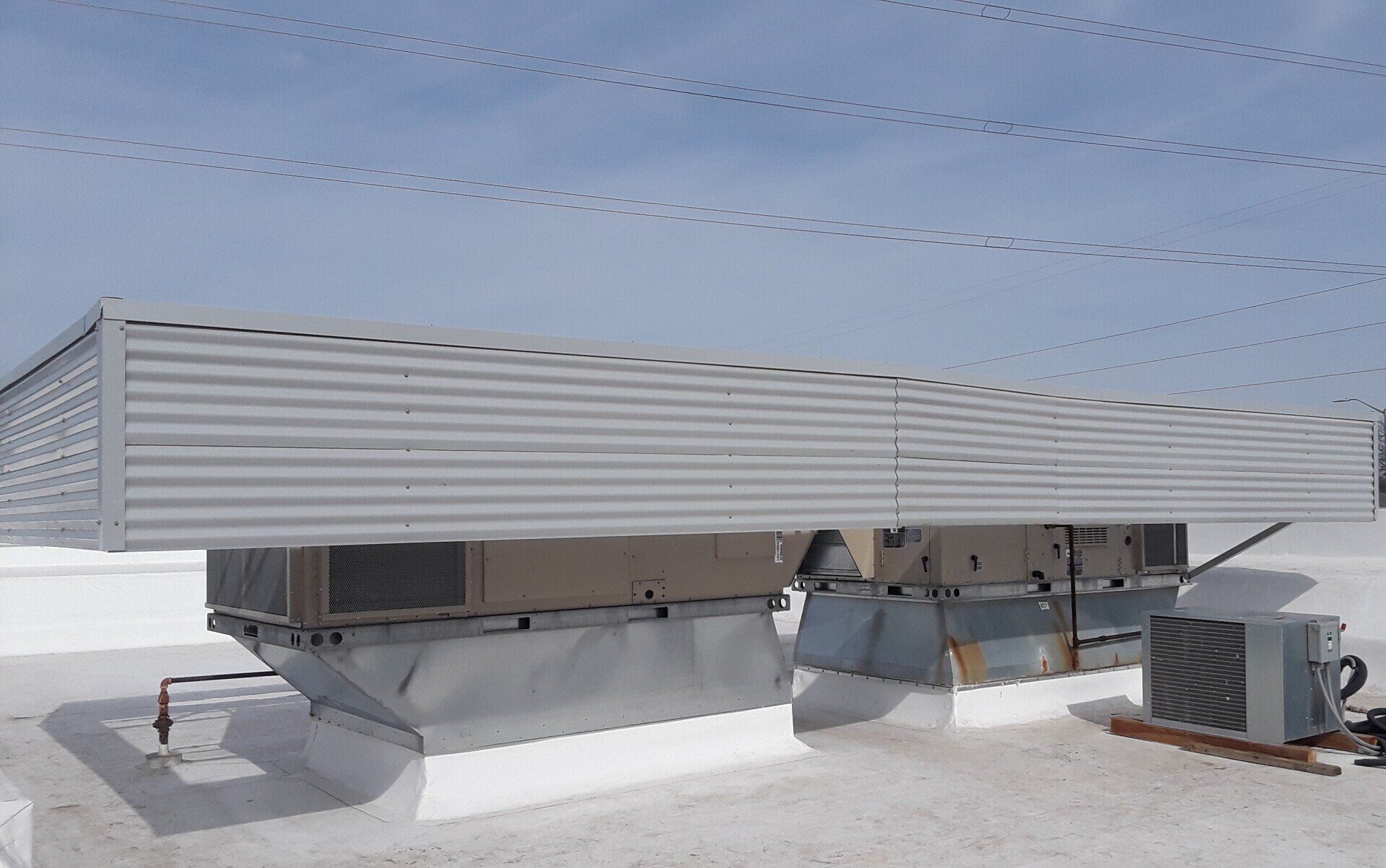Rooftop HVAC units and a large metal ventilation enclosure on a flat roof under a blue sky