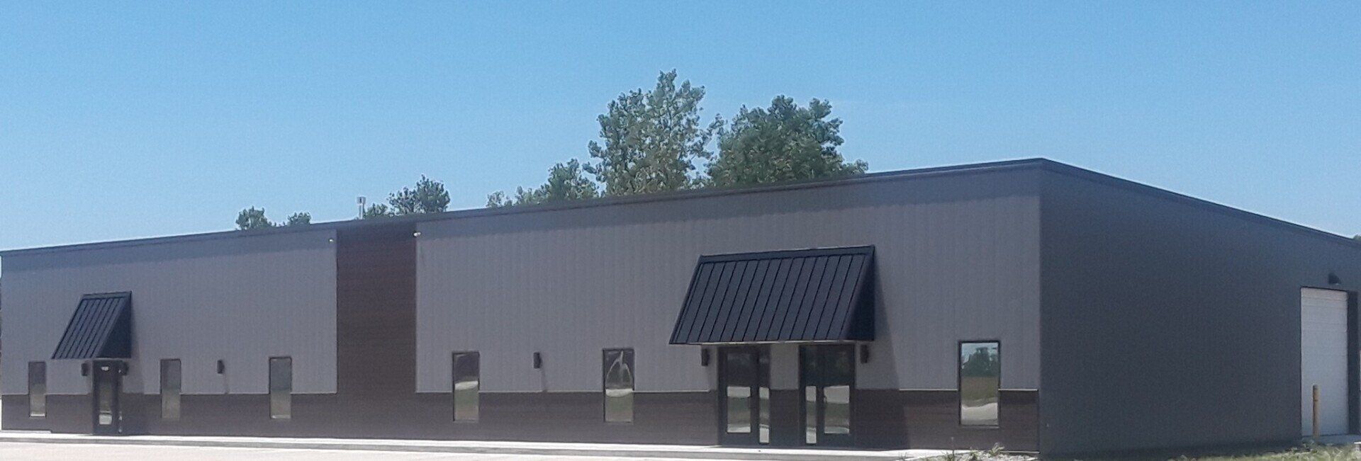 Low brick commercial building with dark awnings and storefront windows under a blue sky