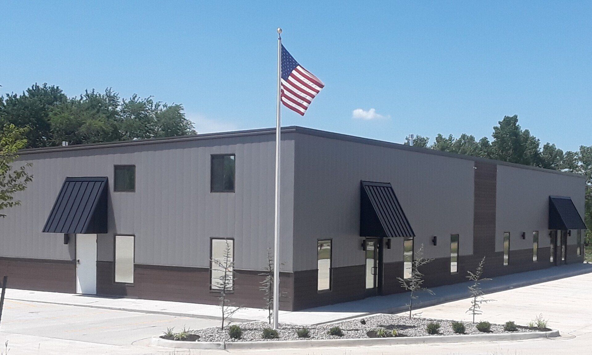 Gray building with black awnings and a flagpole flying an American flag under a sunny sky
