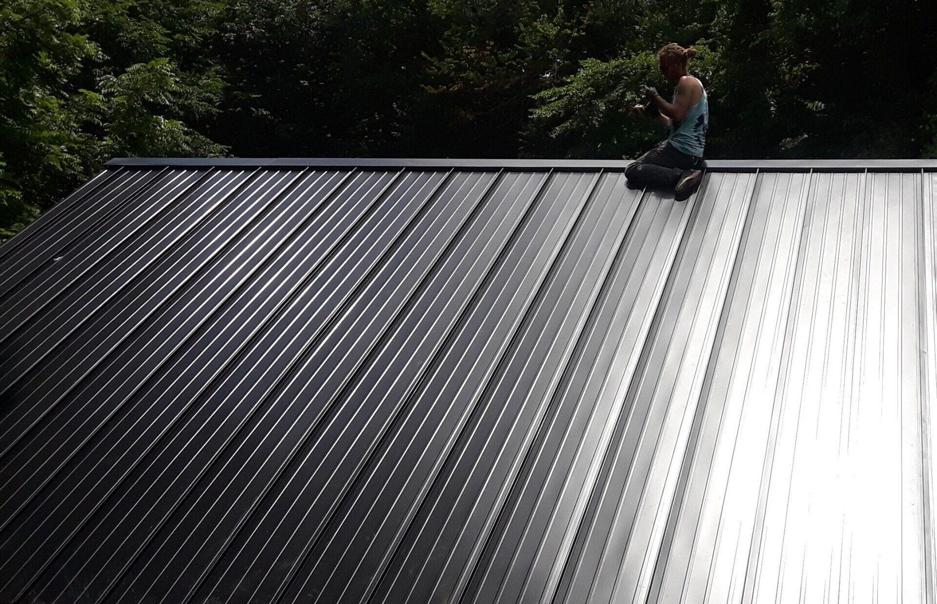 Person sitting on a shiny corrugated metal roof near trees