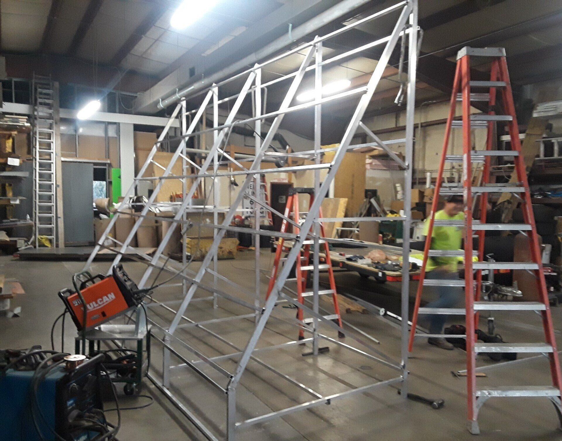 Workshop with a large metal frame under construction, red ladder, and equipment scattered around.