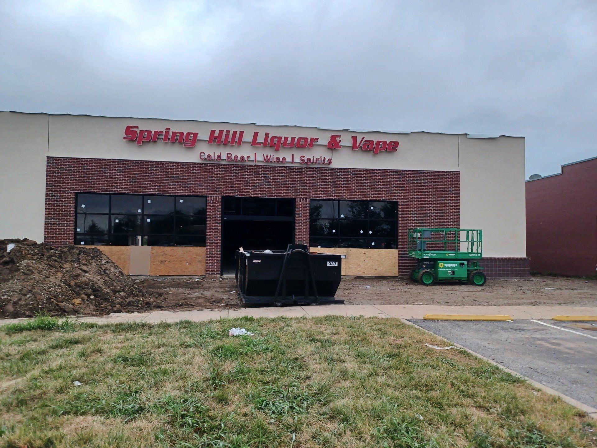Liquor store storefront with boarded windows, a dumpster, and a green construction lift outside
