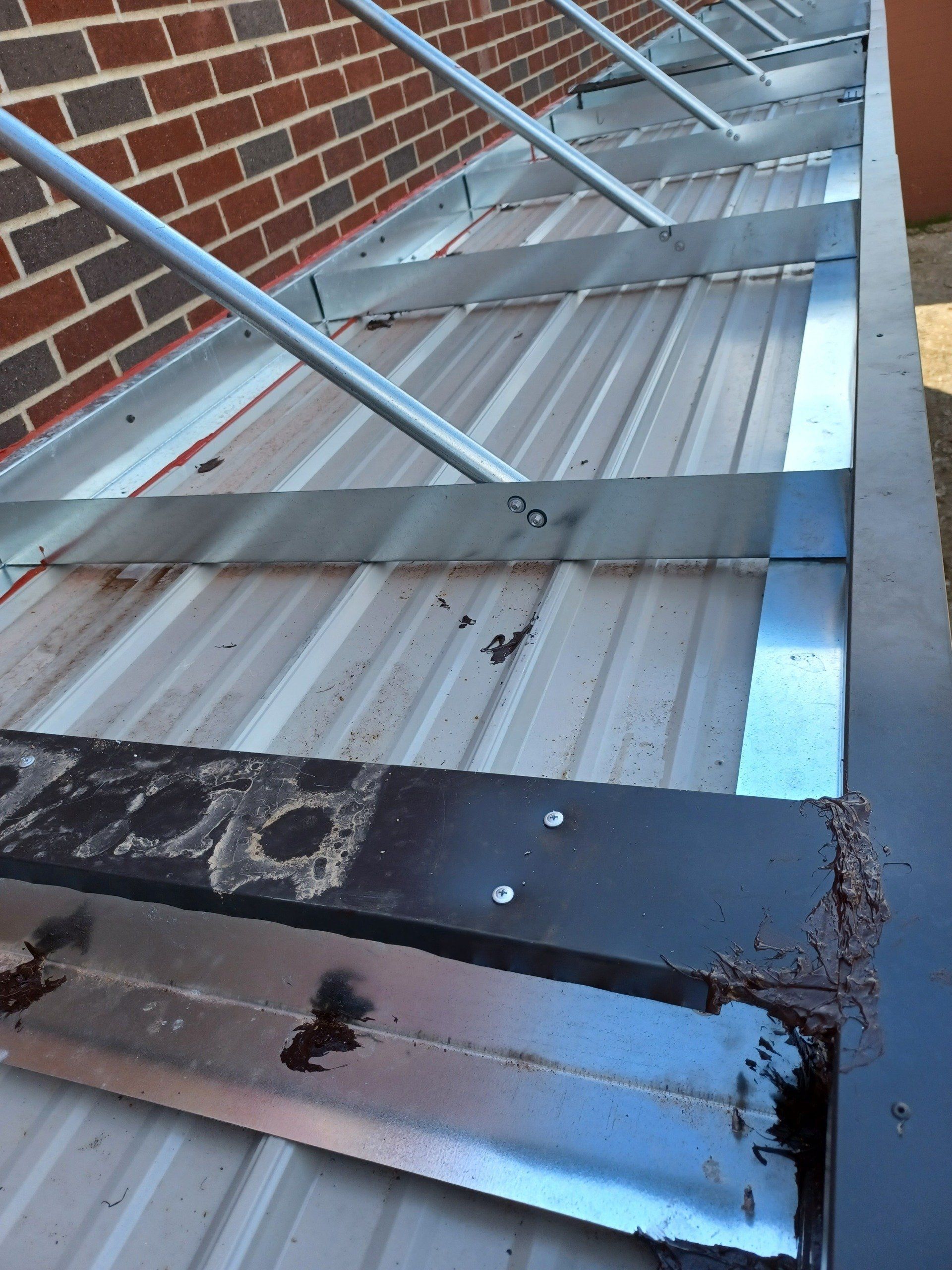 Damaged corrugated metal roof with cracks and debris beside a brick wall