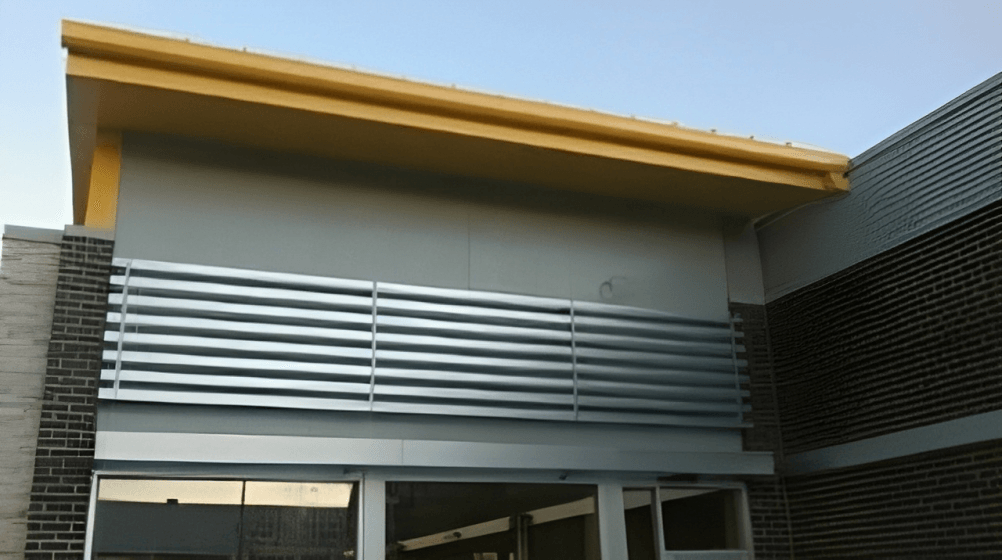 Modern building facade with gray louvered paneling and a yellow roof overhang