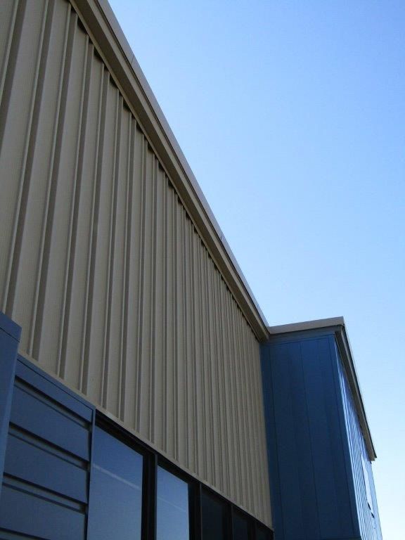 Blue and beige industrial building seen from below against a clear sky.