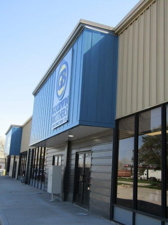 Strip mall storefront with blue and tan exterior and large windows along a sidewalk