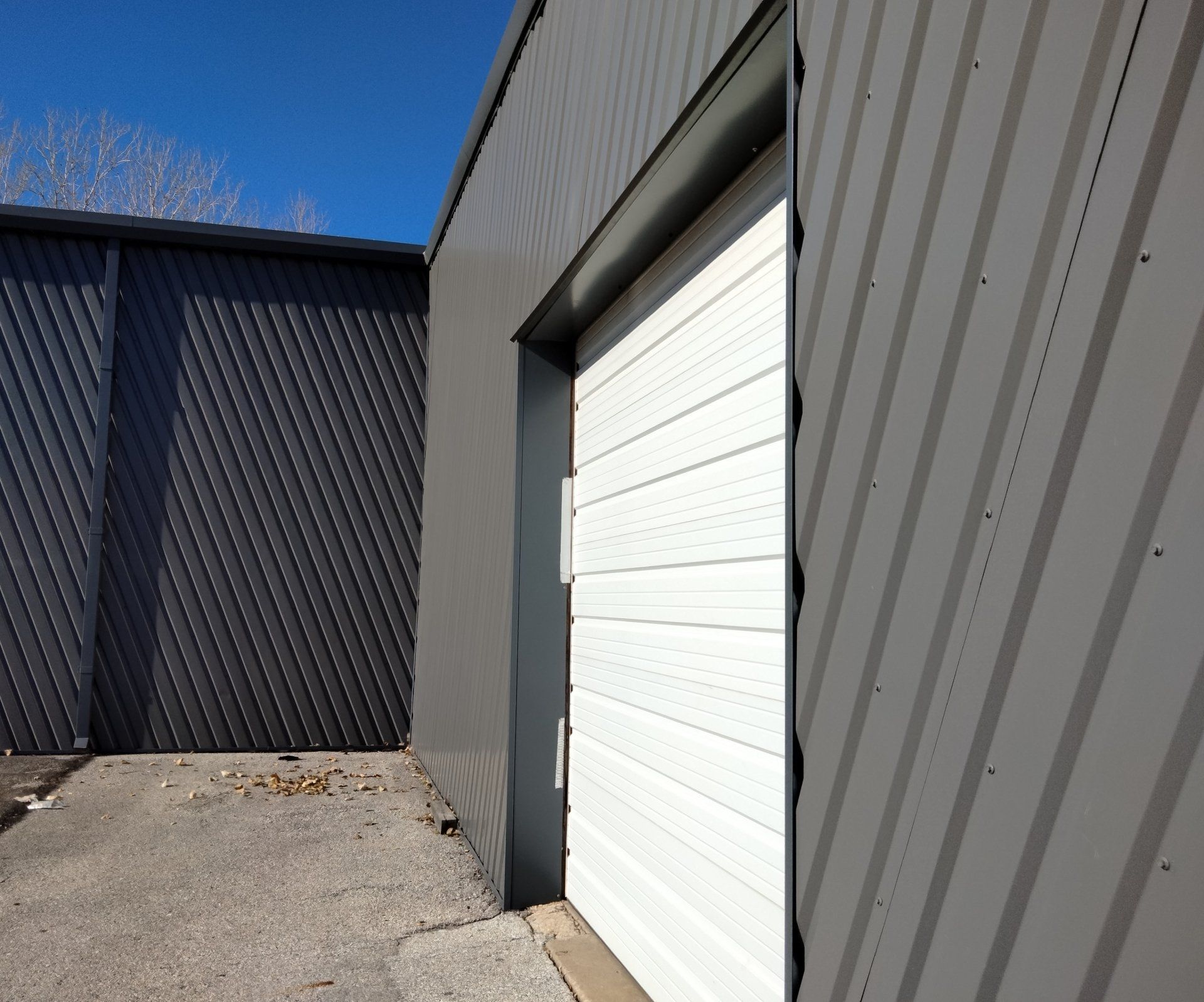 Industrial building exterior with gray metal siding and a white garage door beside a paved alley.
