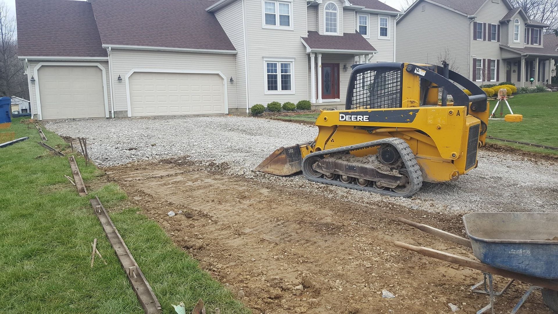 Yellow skid steer grading gravel on a driveway in front of a house.