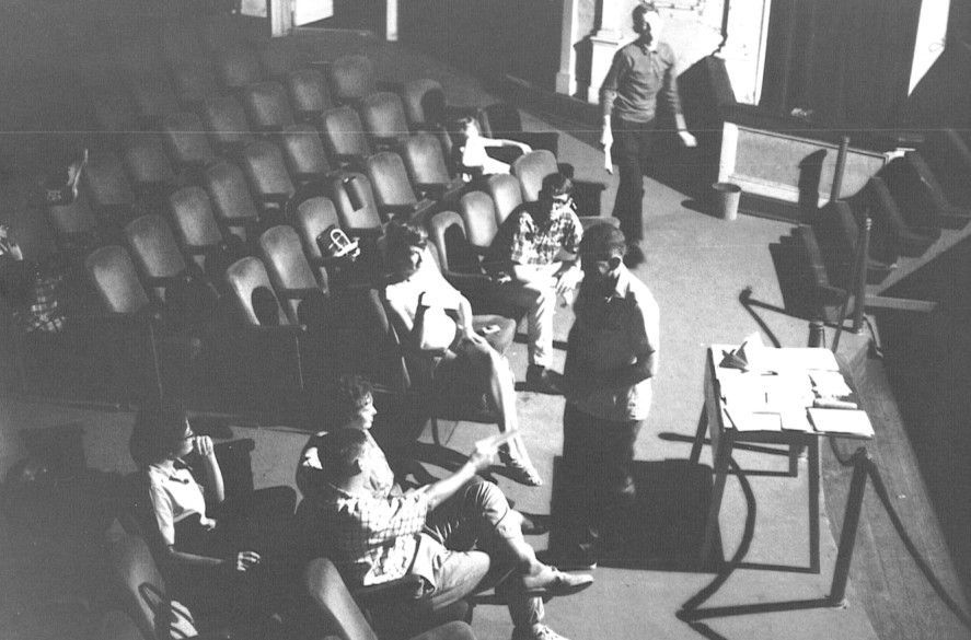 Auditorium with seated people and a person standing near the front beside a table with papers