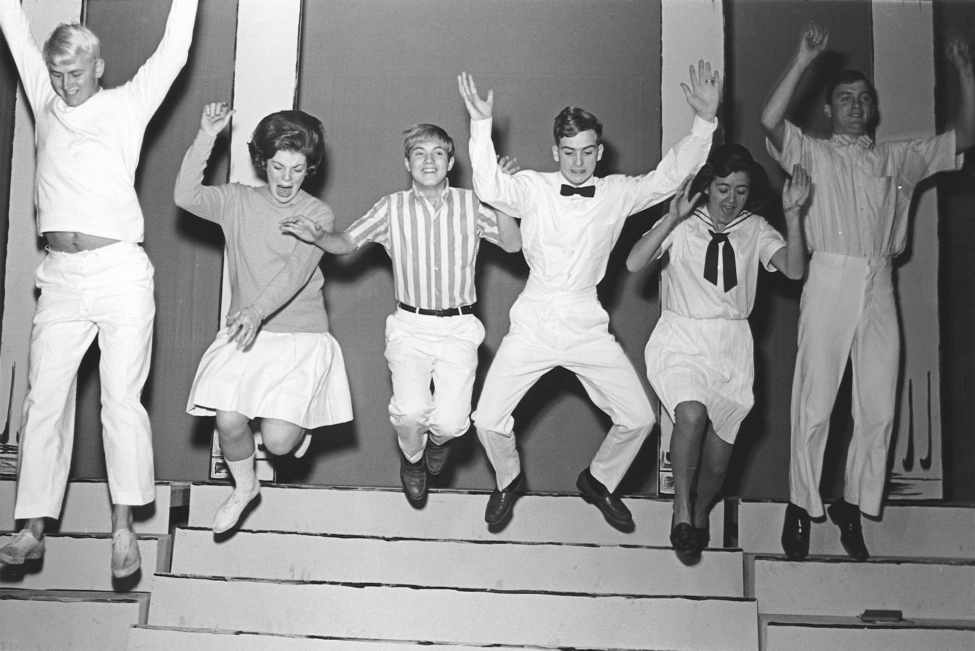 People jumping in unison on a stage, arms raised, in a black-and-white photo