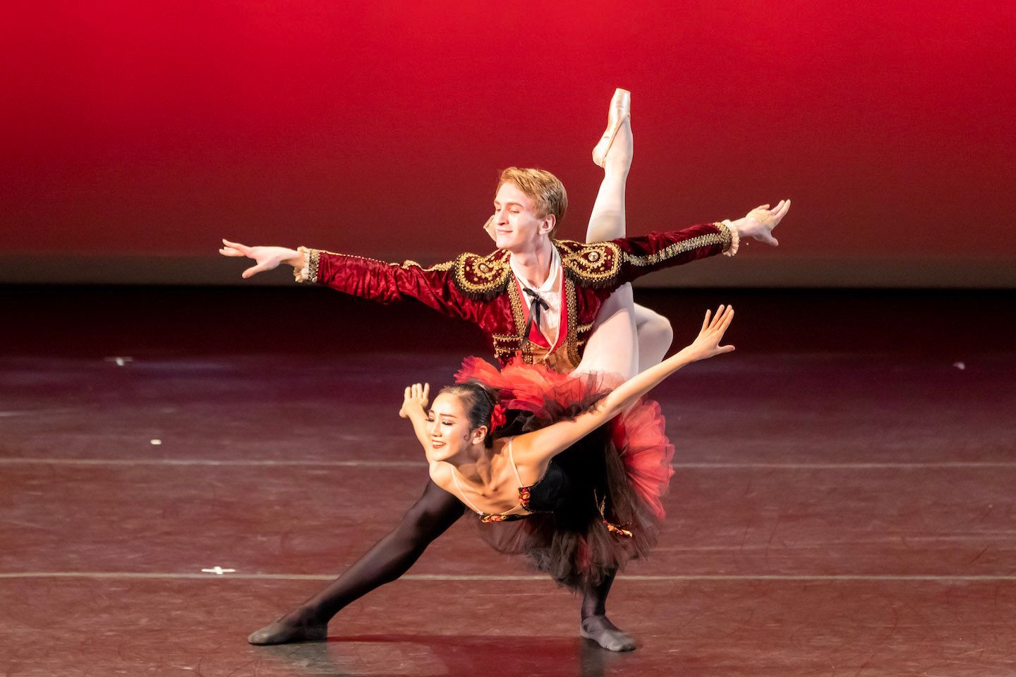 Two ballet dancers in red and black costumes pose in a dramatic stage performance