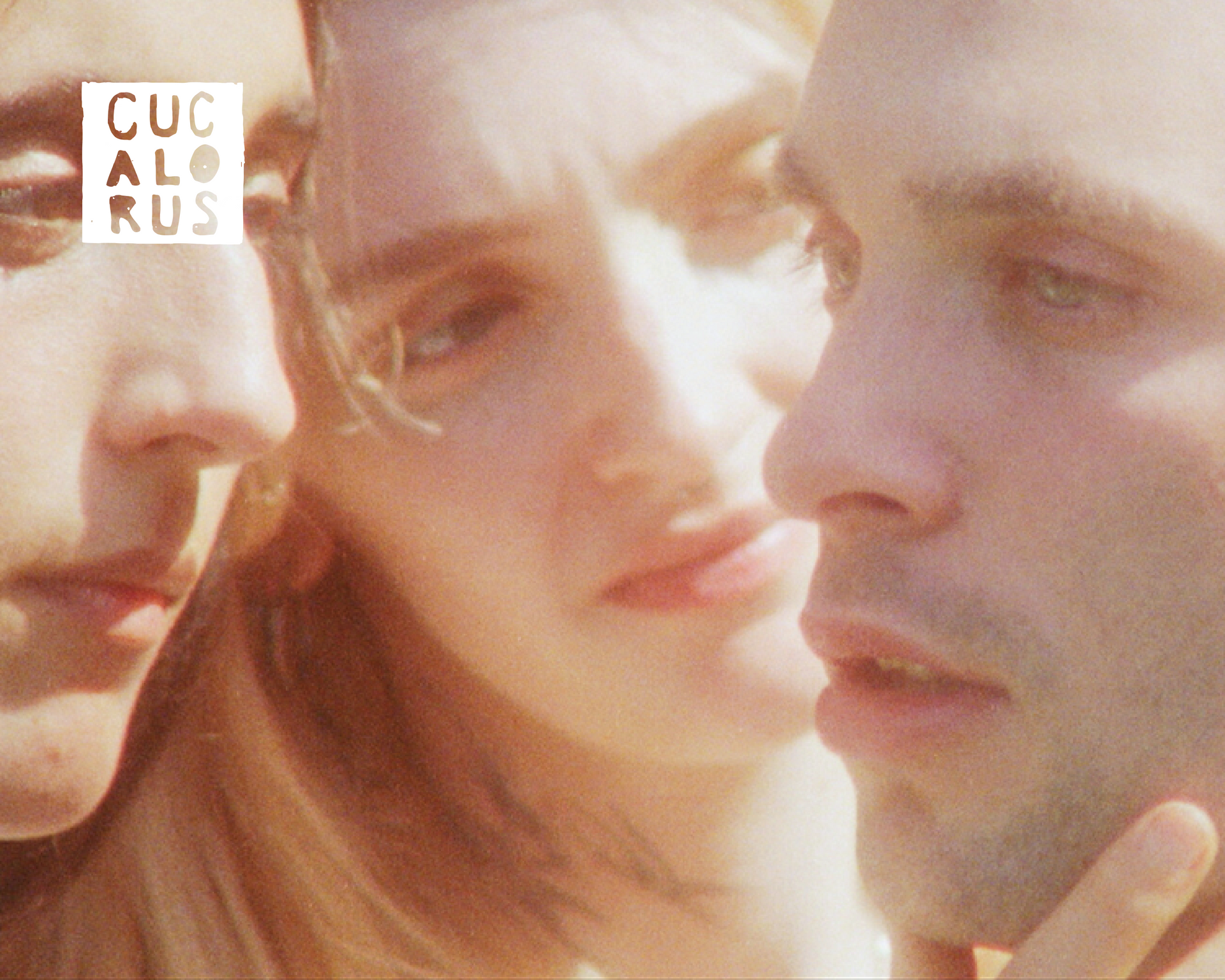 Three softly lit faces in close-up, with a warm, blurred background and a small logo in the corner