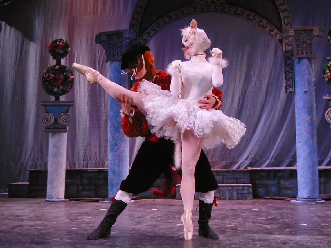 Ballet dancers in white and black costumes performing a dramatic lift onstage