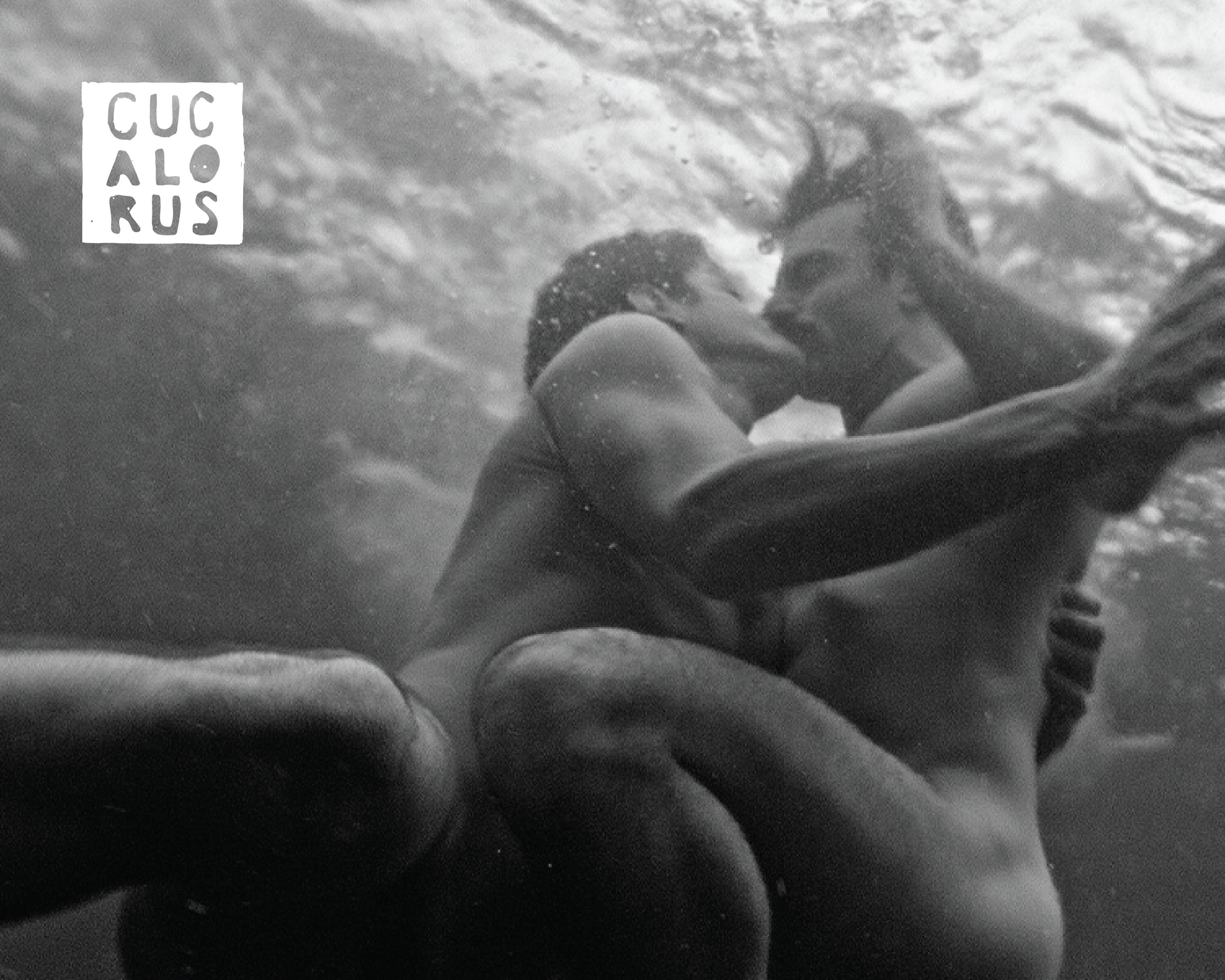 Underwater black-and-white scene of two people embracing, with one leg visible in the foreground.