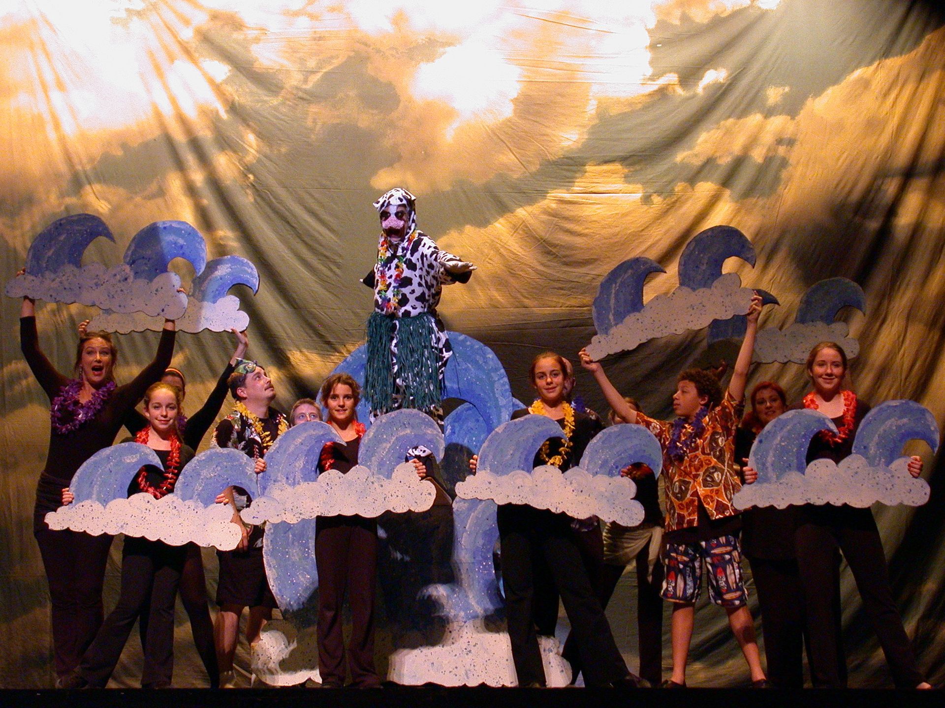 Children performing on stage with blue cloud props and a gold backdrop